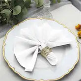 White cloth napkin folded into a bow shape with a decorative ring holder on a scalloped plate with gold trim.