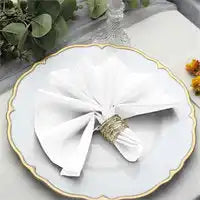 White cloth napkin folded into a bow shape with a decorative ring holder on a scalloped plate with gold trim.
