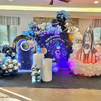 Space-themed balloon arch display with rockets and cosmic decorations illuminated by purple and blue lights.